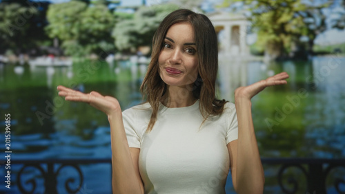 Foto Young hispanic woman with bare hands holding palms up gesture in green park by building; uncertainty
