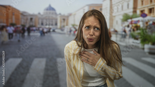 Konstfotografi Young hispanic woman clutching chest with hand on busy city street crosswalk, pleading expression suggesting heartattack; concern pain