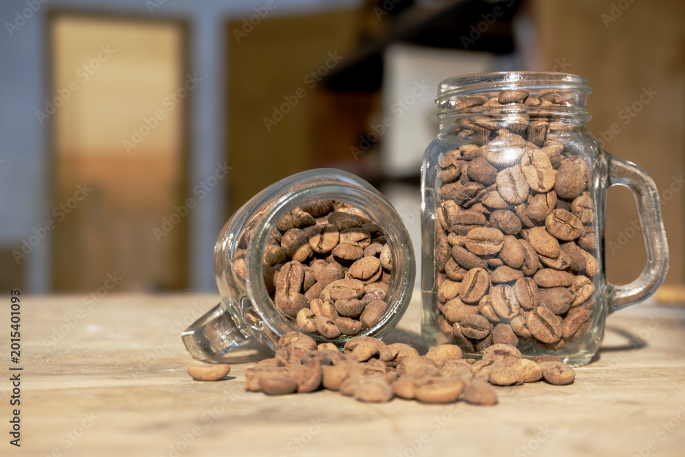 Fototapeta premium Roasted Coffee Beans Spilling from Glass Mason Jars on Wooden Cafe Table