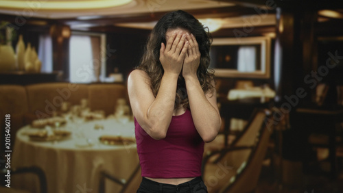 Εκτύπωση καμβά Young hispanic woman anxiously covers face while seated at polished wooden table in elegant restaurant dining area; stress