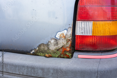 Foto Detail of the rear of an older car with visible corrosion, peeling paint, and moss buildup around the taillight, indicating long-term exposure to the elements