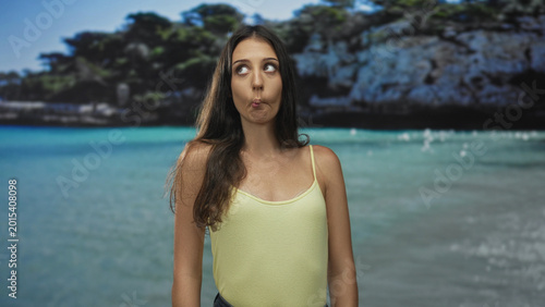 Fotografi Woman making a fish face with puckered mouth at beach, shoulders exposed and looking up toward sky; playful summer moment