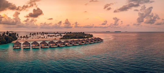 Fotobehang Cappuccinokleur Breathtaking aerial view of Maldives water villas at sunset over a peaceful ocean luxury summer resort picturesque travel landscape wallpaper with serene turquoise sea and golden hour sky panorama  © icemanphotos