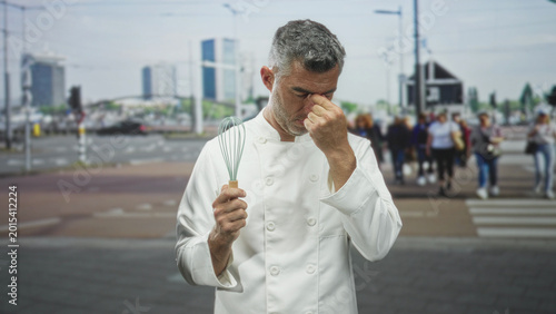 Foto Middle age chef man in white jacket pinching nose and holding whisk on street crosswalk near buildings; stress