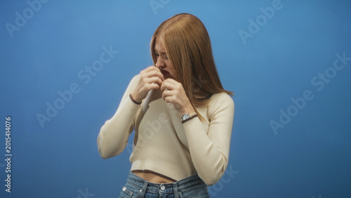 Fényképezés Redhead woman in beige sweater and jeans touching nose with both hands and clutching chest in studio against blue backdrop; disgust reaction