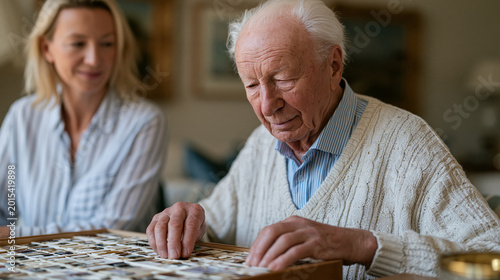 Elderly male Alzheimer patient in luxury memory care common room arranging familiar objects from life history box on table, trained reminiscence therapy specialist seated quietly beside him with gen