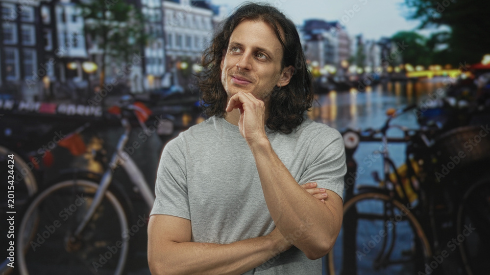 Fototapeta premium Man with hand on chin and closed eyes on amsterdam street by canal with bicycles and water reflections; thoughtful introspection.