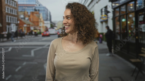 Foto Woman smiling with curly hair and relaxed posture on a city street, casual shirt visible; everyday confidence