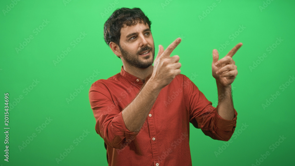 Fototapeta premium Man with beard points fingers with both hands toward right in studio green screen; playful presentation.