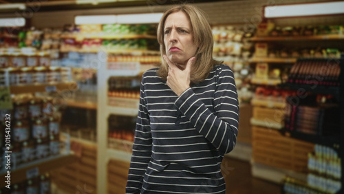 Quadro su tela Woman touching chin and frowning while inspecting grocery products in a building; doubt thought pondering