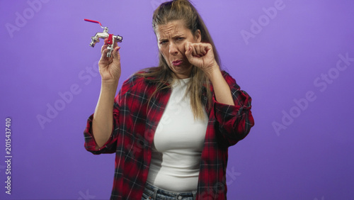 Foto Woman holding metal faucet with red handle, pinching nose and grimacing while sticking out tongue in studio; disgust rejection