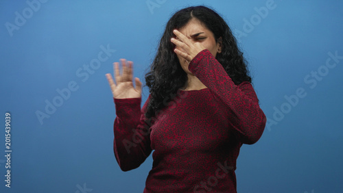 Tableau sur toile Young arab woman pinching her nose and waving a hand in a blue studio, reacting to an unpleasant odor and closing eyes; disgust