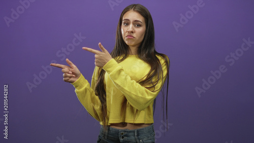 Schilderij op canvas Teenage girl points fingers in a dismissive finger gun gesture wearing yellow crop sweater and jeans in studio; uncertainty