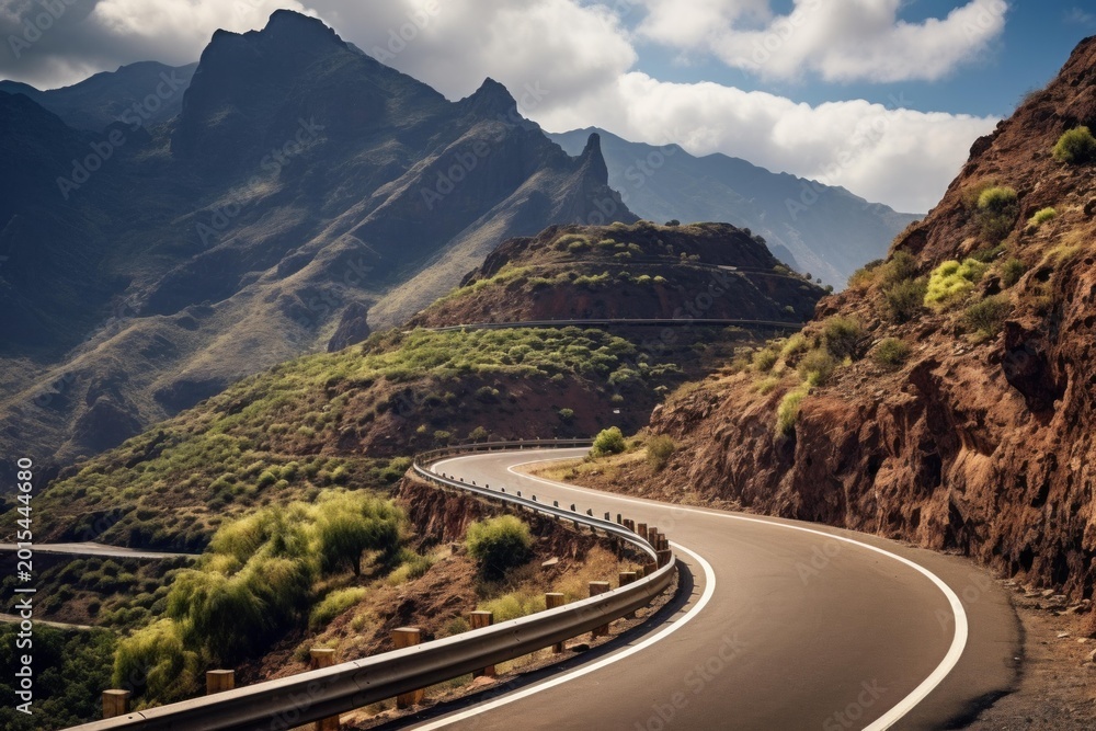 Fototapeta premium Asphalt highway curving through arid mountains and green shrubland under a blue sky