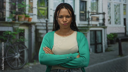 Valokuva Woman with crossed arms and pursed lips on a city street in front of townhouse building wearing green cardigan; disapproval stubbornness