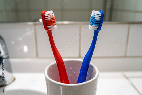 Two toothbrushes in a glass red and blue bathroom setting