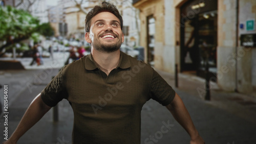 Photos Man smiling with arms outstretched on a crowded street by a stone building, head tilted back and eyes closed; joy celebration