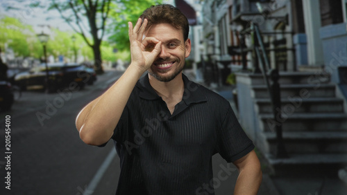 Fotografía Man smiling with bare forearms and hands on hips on a street near building steps; confidence approachability