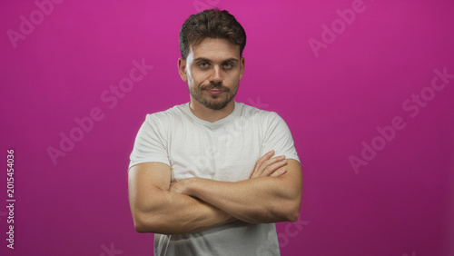 Fotografie Young hispanic man with crossed arms and beard in a pink studio, eyes closed with a smug expression; confidence attitude
