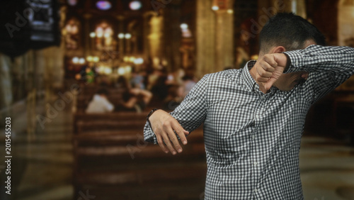 Cuadro en lienzo Man with moustache covers face with forearm and gestures with open hand inside ornate building with pews and chandeliers; awkwardness
