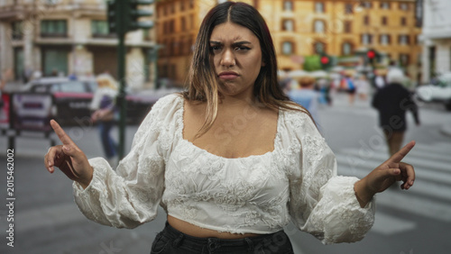Cuadro en lienzo Woman in white embroidered blouse with hands raised and pointing finger while frowning at traffic in a busy city street; frustration