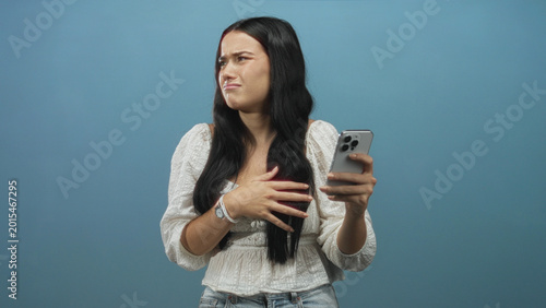 Cuadro en lienzo Woman holding smartphone with palm out and pained face rejecting screen content in studio; disgust rejection