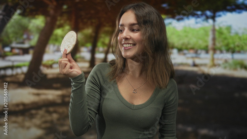 Schilderij op canvas Woman holding ricecake between two fingers in forest park outdoors, smiling at camera; playful curiosity