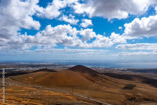 Scenic view of a Lanzarote village nestled at the foot of a volcanic hill under a dramatic cloudy sky. The contrast of white buildings against the rugged terrain highlights Lanzarote unique landscape