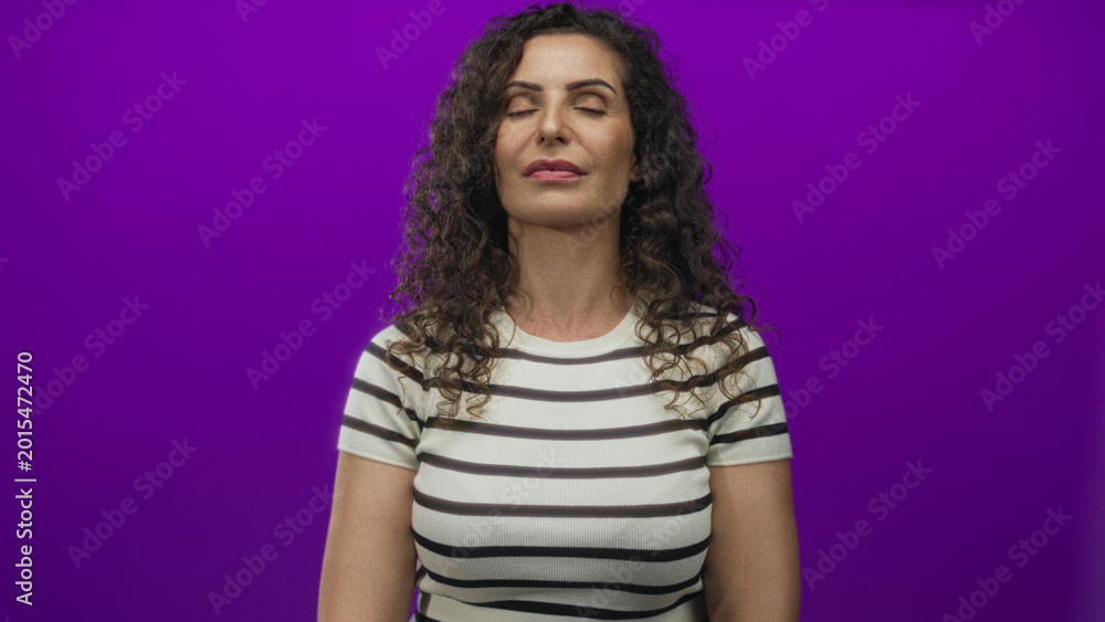 Obraz premium Hispanic woman wearing white striped shirt standing calmly with closed eyes in purple studio; inner calm.
