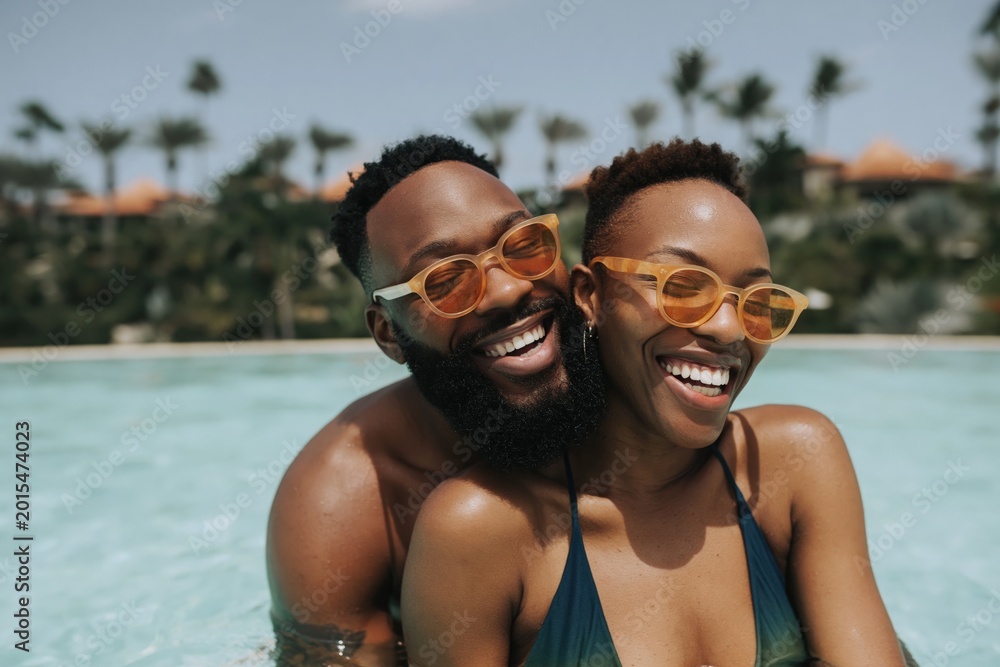 Obraz premium Black couple laughing while hugging in resort swimming pool