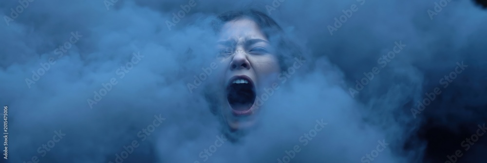 Fototapeta premium Woman screaming amid dense blue smoke in dim studio environment