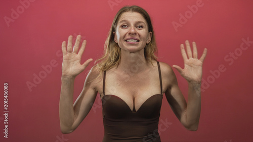 Foto Woman showing bare breasts with hands raised palms forward wearing brown camisole in studio pink backdrop; playful openness