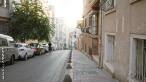 Blurred urban street scene with defocused sidewalk and parked cars, soft bokeh on distant buildings street; background copyspace calm.