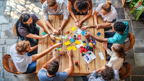 Teamwork, Collaboration, and Brainstorming Session: Diverse Group of Young Professionals Engaging in Creative Problem-Solving with Colorful Sticky Notes and Markers Around a Wooden Table.