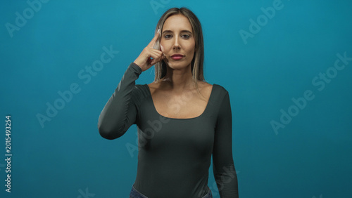 Canvas Print Woman pointing index finger up in teal studio backdrop with direct gaze and raised hand; confidence focus decisive intent