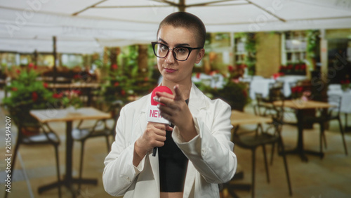 Foto Woman reporter holding red microphone pointing finger in street cafe patio setting; assertive confidence