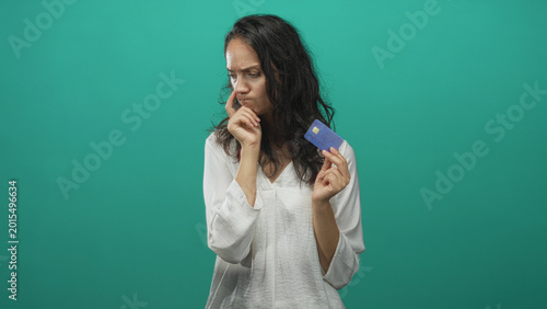 Foto Woman holding blue creditcard with hand on chin, frowning and examining the card in studio; financial worry