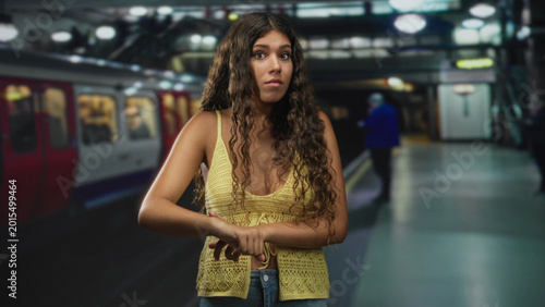 Tableau sur toile Hispanic woman points finger to wrist showing exposed chest by a metro train in an underground building; impatience waiting