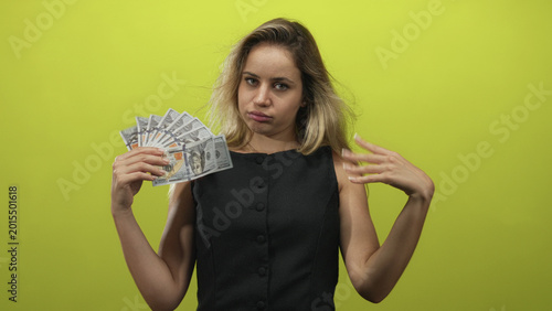 Canvas Print Young blonde woman holding a fan of dollar bills with hand raised fanning cash in a green studio; indifference wealth