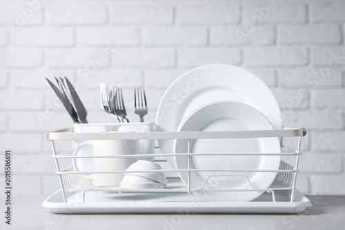 Canvas Print Set of clean dishes and cutlery in drying rack on light grey table, closeup