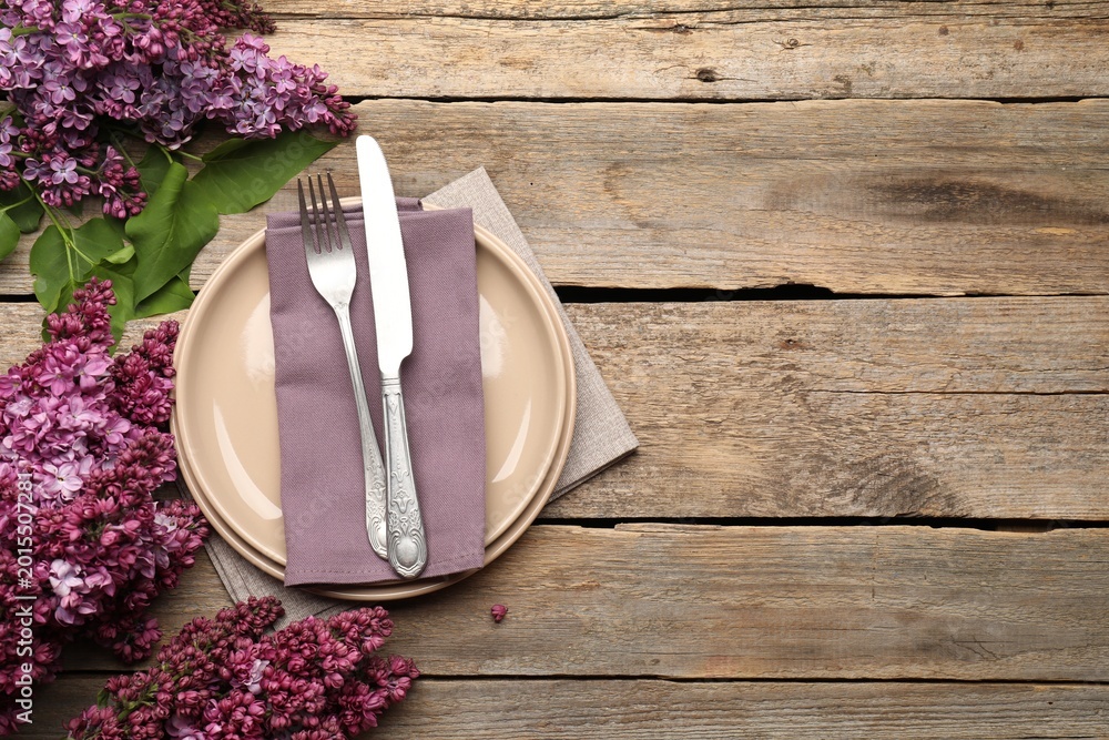 Fototapeta premium Stylish setting with plates, cutlery, napkin and flowers on wooden table, flat lay. Space for text