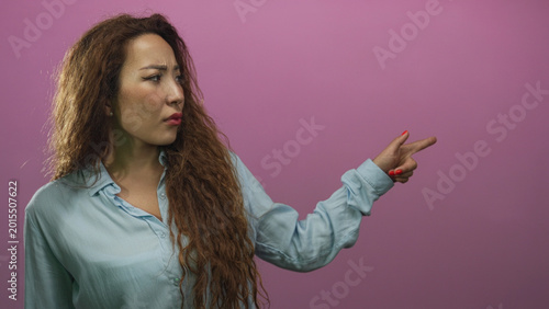 Foto Woman pointing finger with visible hand and raised arm in pink studio while glancing left with furrowed brow; disapproval