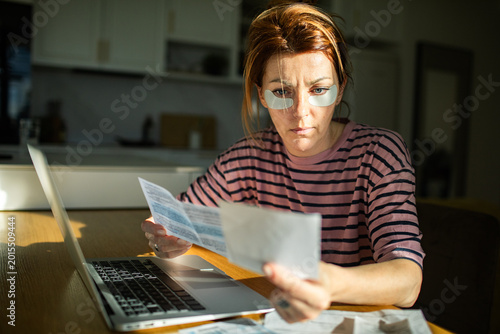 Woman with under eye patches reviewing bills at home