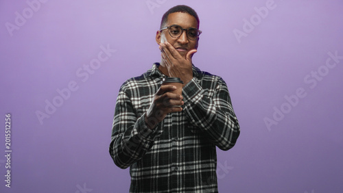 Canvas Print Man in glasses and plaid shirt holding a takeaway coffee cup, hand to chin and touching cheek while smiling in studio; thoughtful calm introspection