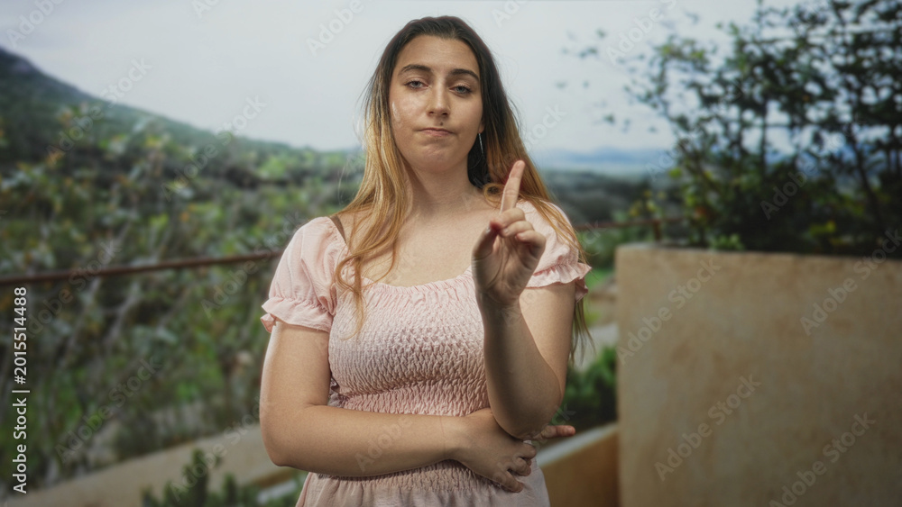 Fototapeta premium Woman pointing index finger with crossed arms on a building balcony overlooking hills, warning gesture; disapproval.