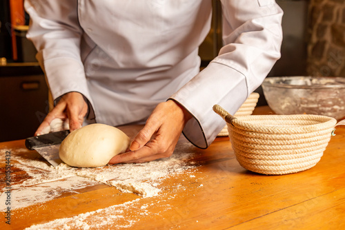 Chef cortando massa artesanal sobre bancada de madeira enfarinhada em cozinha