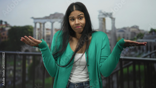 Cuadro en lienzo Young latin woman shrugs open palms with puzzled expression in front of ancient building ruins; uncertainty