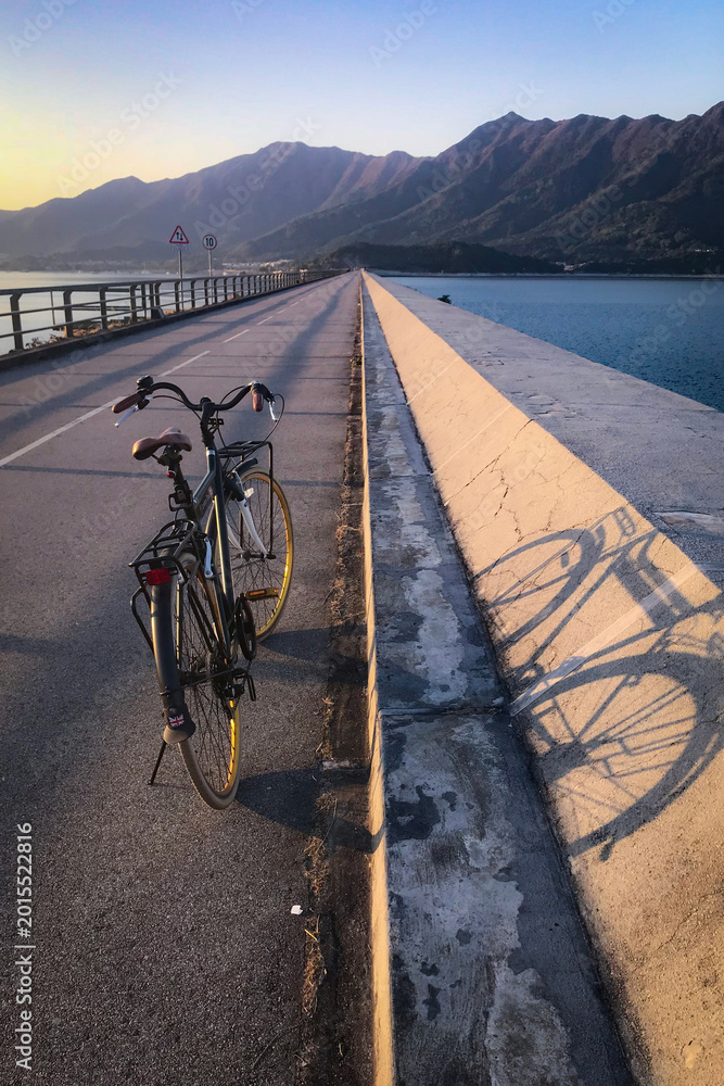 Fototapeta premium Retro bicycle parked on a scenic coastal road with mountains in the background at sunset