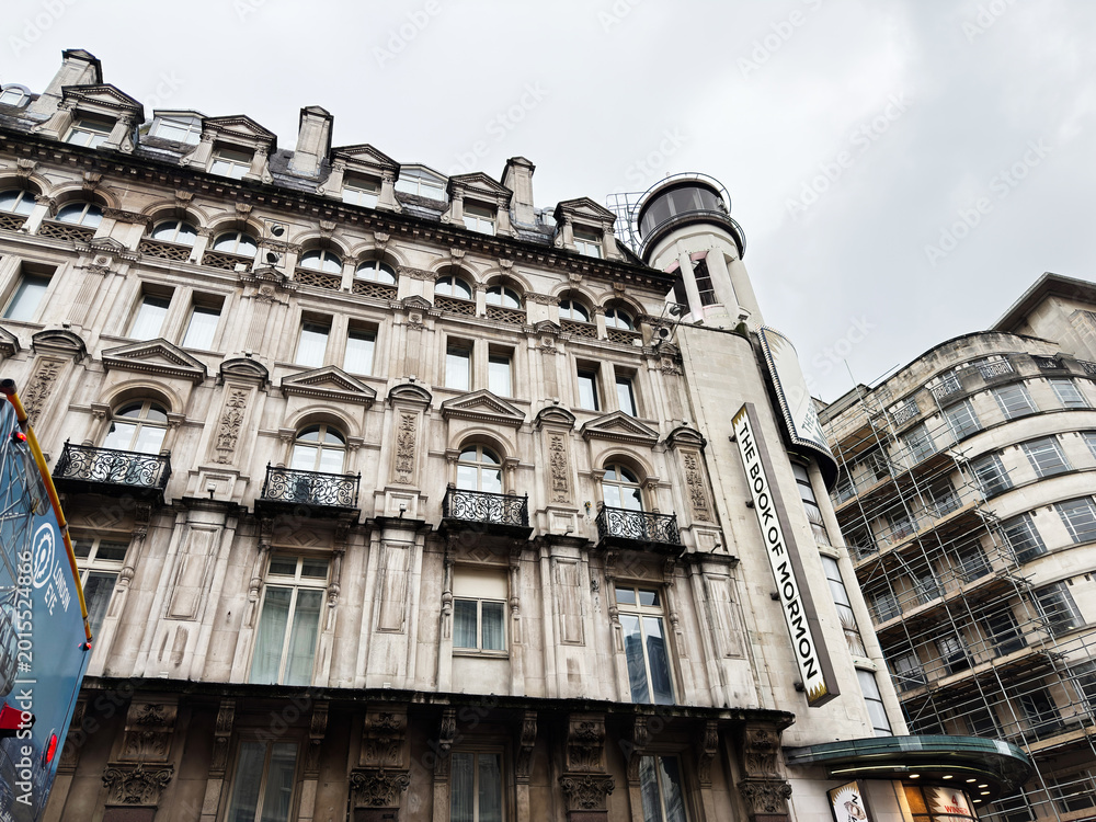 Obraz premium Historic theatre facade with The Book of Mormon sign on ornate stone building in London, UK showing Victorian architecture and urban streetscape under overcast sky