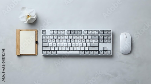 White mechanical keyboard and wireless mouse on gray concrete desk with bamboo notepad and orchid flower, minimalist workspace flat lay.